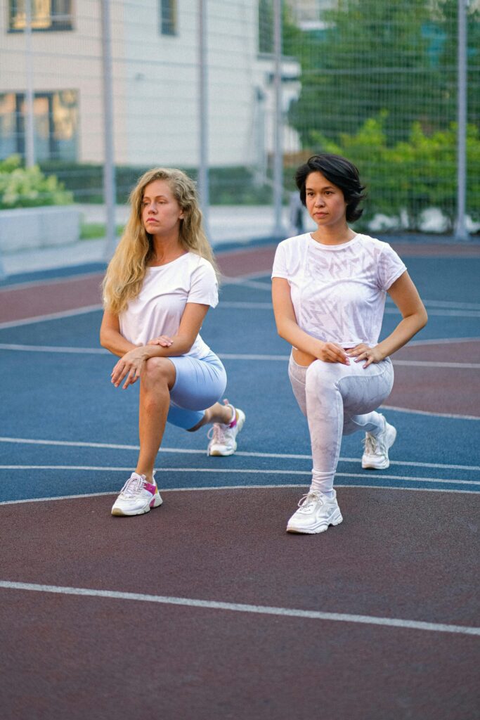 Confident ladies stretching legs on sports ground